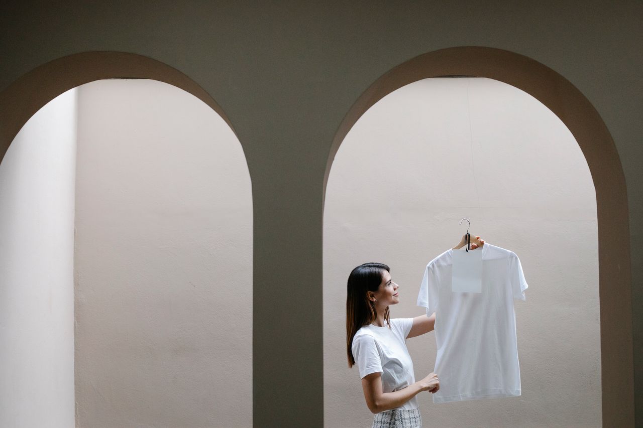 Side view of happy young female designer with long dark hair standing in spacious house with arched walls and showing white t shirt